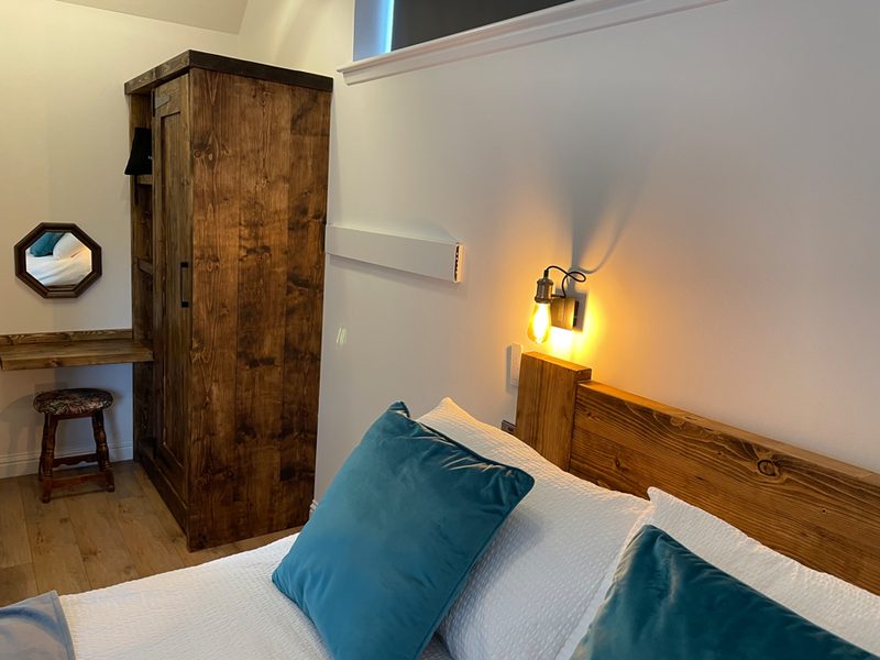 Slaapkamer met houten bed, petrolkleurige kussens en een wandlamp naast de kast