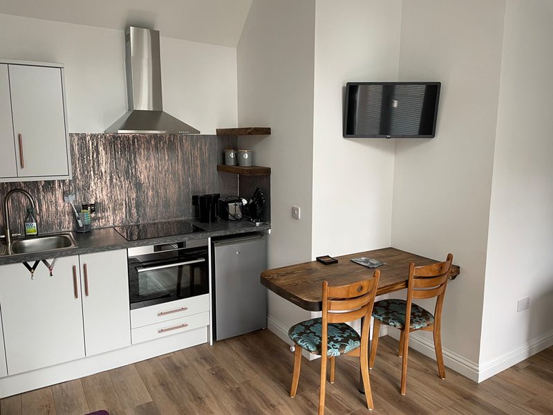 Houten eettafel voor twee naast de keuken, met een televisie aan de wand