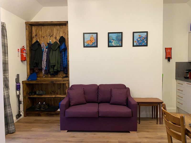 Entree met kapstok, pruimkleurige slaapbank en drie ingelijste vlinderprenten aan de wand